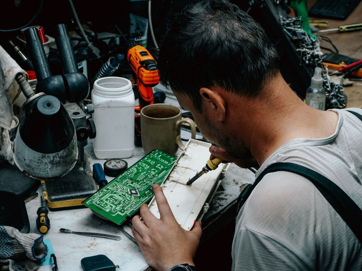 Technicien réparant une carte électronique sur un établi encombré