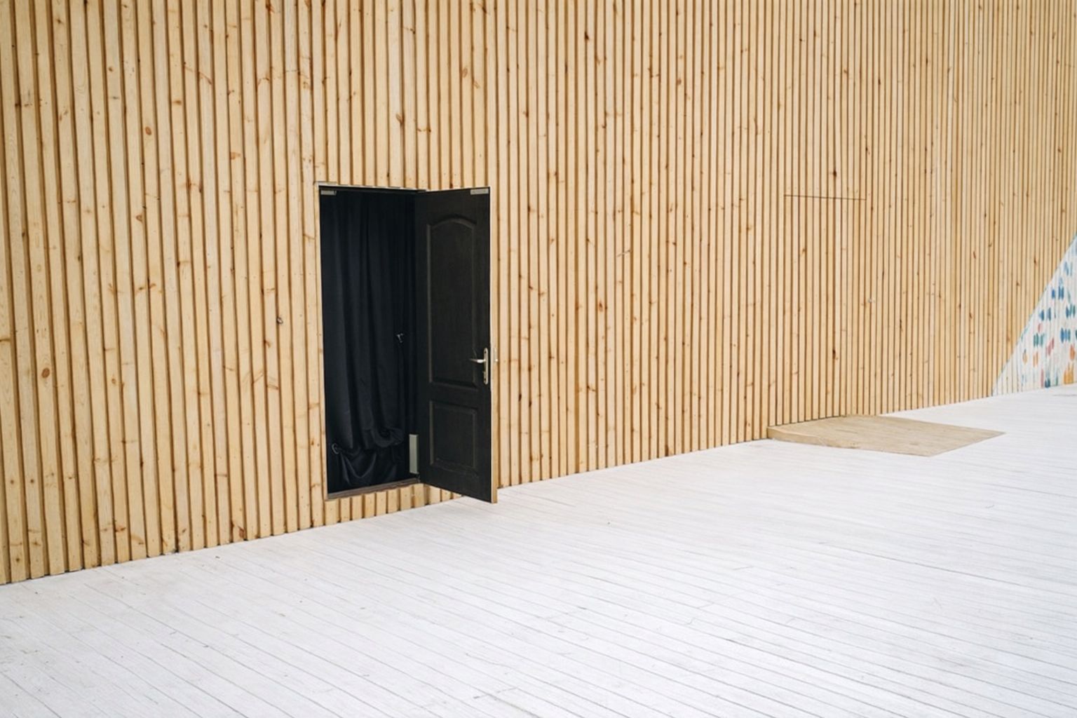 Mur en tasseaux de bois clair avec porte noire ouverte.